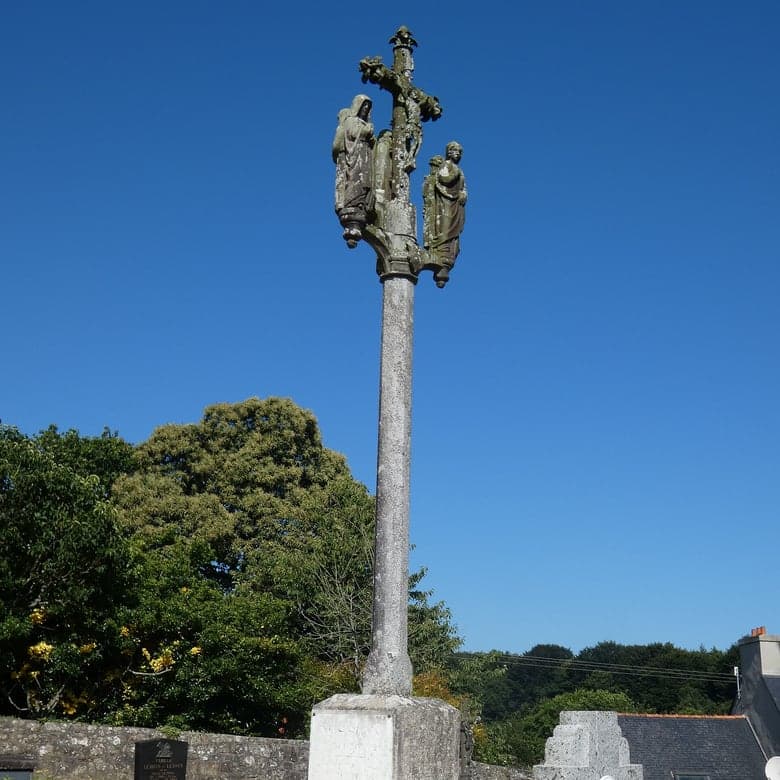 Un calvaire de granit breton dressé sur son fût, personnages sculptés au sommet.