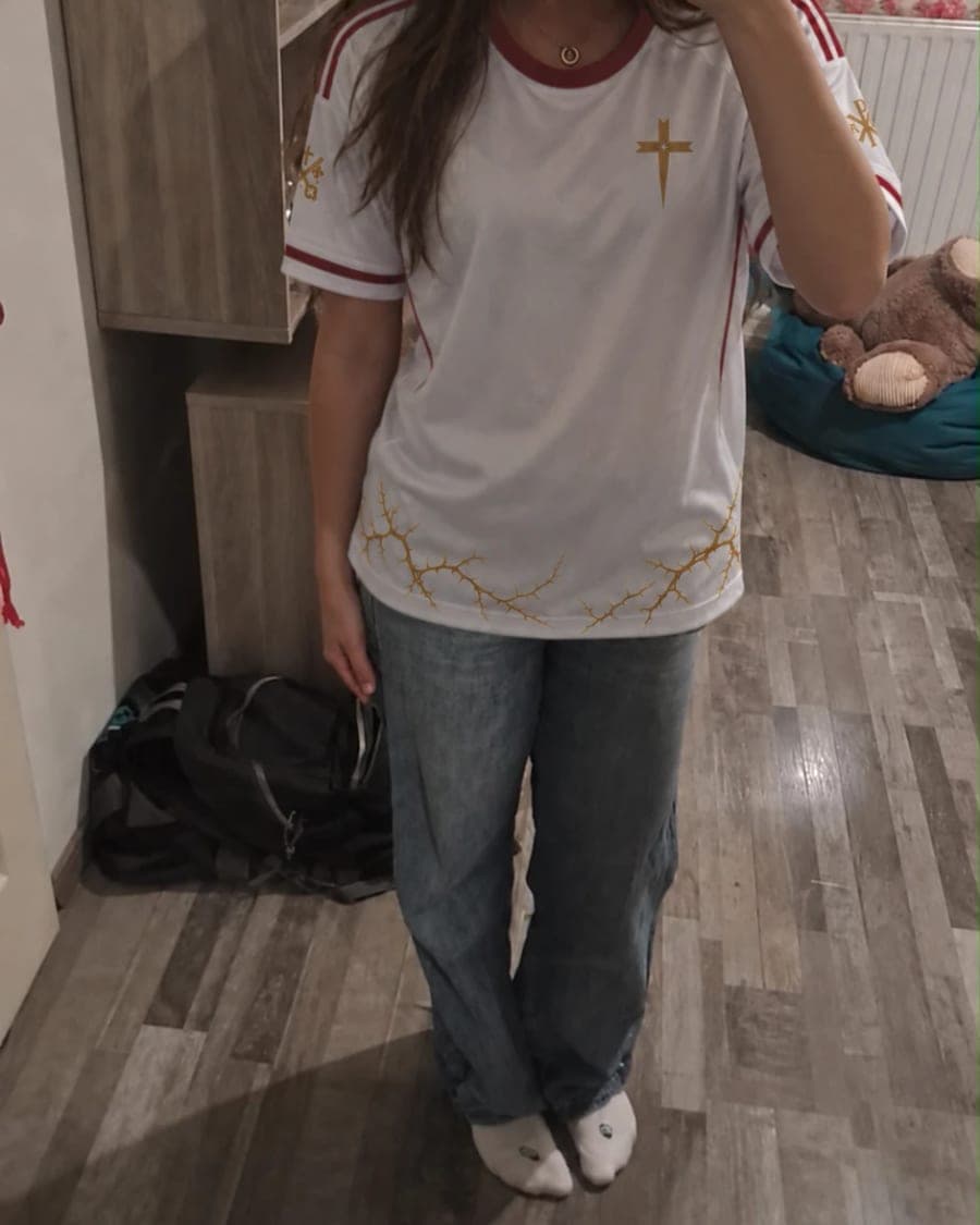 Le maillot porté de face devant un miroir, croix dorée côté cœur et couronne d’épines sur le bas.